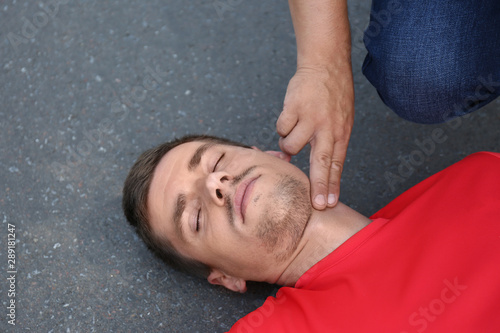 Passerby checking pulse of unconscious young man outdoors photo