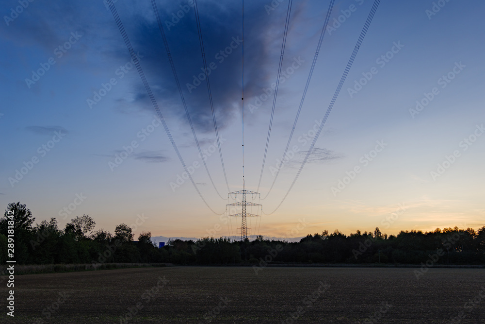 Outdoor silhouette scenery of High Voltage Tower and Wires over agricultural field in countryside area and background of twilight sunset sky.