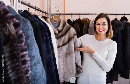 Woman choosing short coffee-colored fur jacket in women’s cloths store © JackF