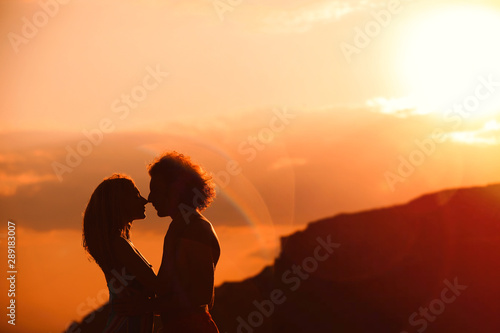 Young woman in bikini and her boyfriend on beach at sunset. Lovely couple