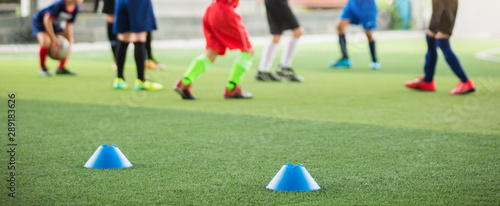 Fototapeta Naklejka Na Ścianę i Meble -  selective focus to blue marker cones are soccer training equipment on green artificial turf with blurry kid players training background. material for training class of football academy.