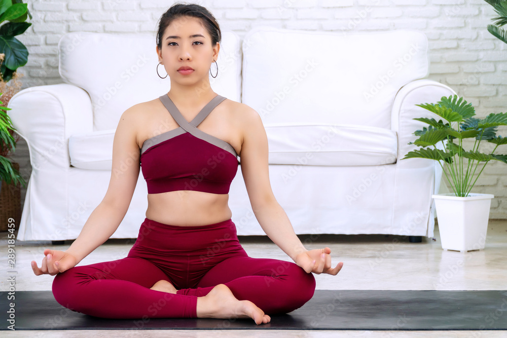Activity young women wear red sportswear sitting on mat in front of white sofa while doing position yoga in living room. Relaxation girl practice advanced yoga at home. Lifestyle healthy concept. Activity young women wear red sportswear sitting on mat in front of white sofa while doing position yoga in living room. Relaxation girl practice advanced yoga at home. Lifestyle healthy concept.