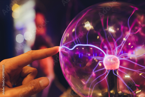 Hand touching a plasma ball with smooth magenta-blue flames. photo