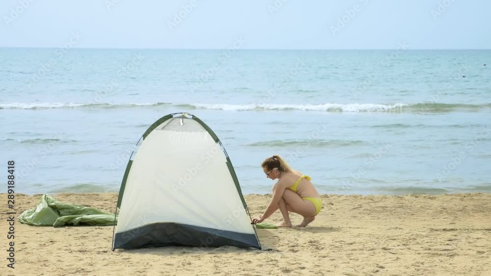 girl in a swimsuit puts up a tent for camping on a sandy beach against the sea in the summer girl in a swimsuit puts up a tent for camping on a sandy beach against the sea in the summer