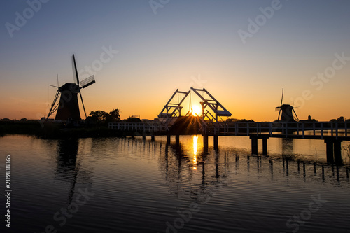 Traditional Romantic Dutch Windmills and Wooden Drawbridge in Kinderdijk Village in the Netherlands. Picture Taken At Golden Hour