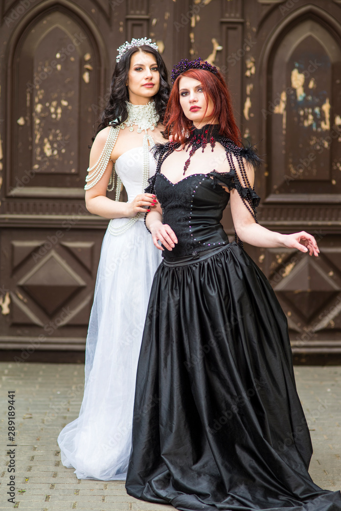 Portrait of Two Girls Together Standing Embraced Outdoors. Posing in Black and White Dresses.  Wearing Diadems.