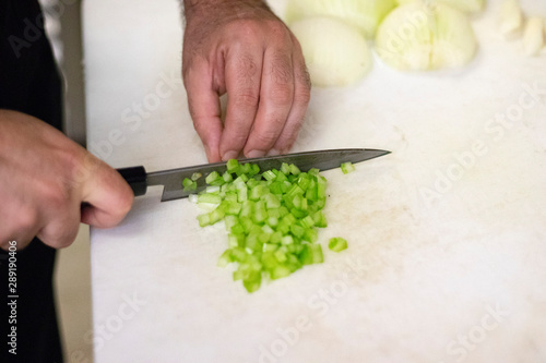 Closeup on a cook man chopping celery and white onions with a kitchen knife in his Vancouver restaurant kitchen