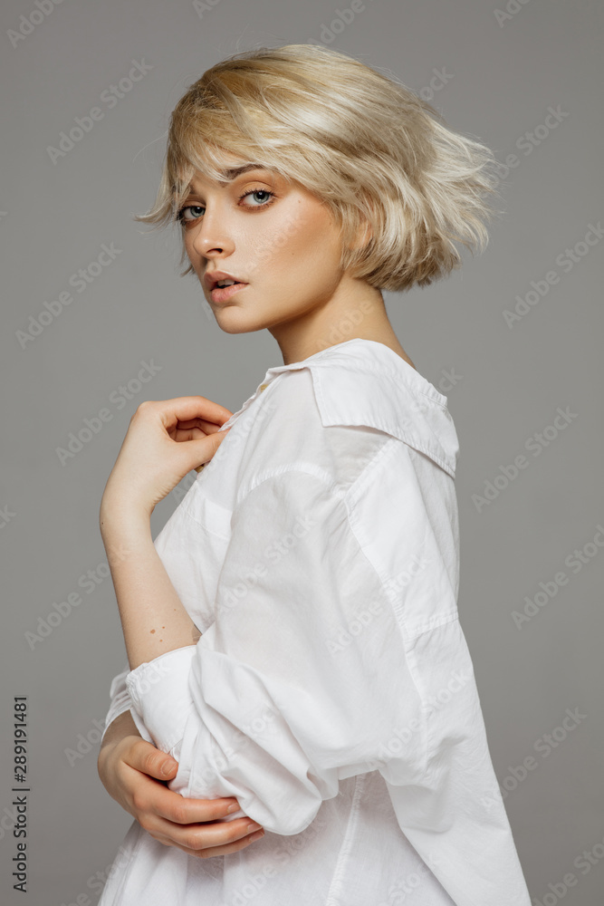 Portrait of beautiful blonde woman in white shirt and fashionable hair - obrazy, fototapety, plakaty 