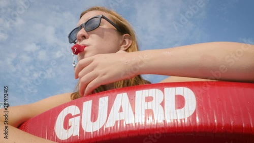 Lifeguard blowing a whistle at a swimmer at a public pool. A red float stands out against the blue summer sky. Authentic shot represents summer activities, employment and safety.