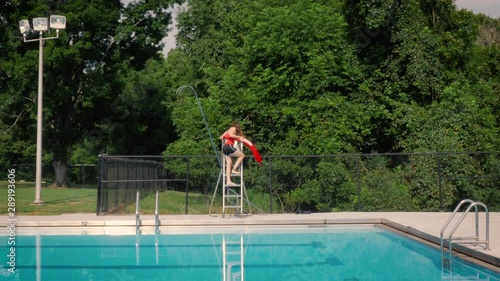 Wide shot of a lifeguard climbing onto a guard tower at a public pool. The teen starts her shift working a summer job lifeguarding. Action shot represents summer activities, employment and safety.
