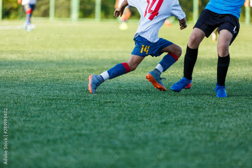 Boys in white and blue sportswear plays  football on field, dribbles ball. Young soccer players with ball on green grass. Training, football, active lifestyle for kids concept 