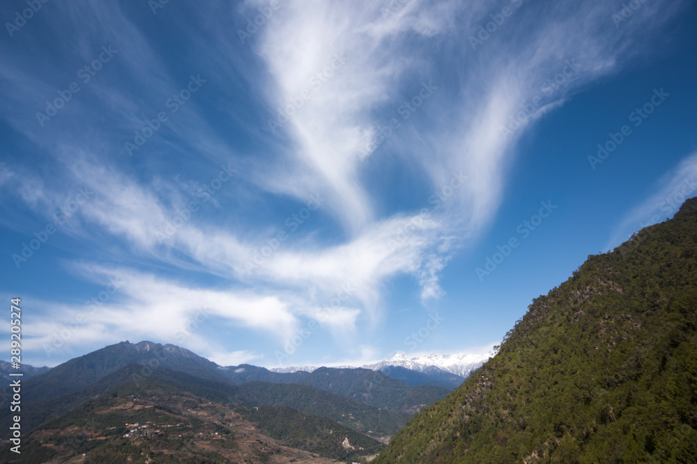 White wispy clouds, blue sky with mountain background