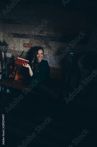 beautiful girl in a green dress reading a book. Art: the book, the violin, the lights. The concept of advertising musical instruments, fashion, symbols, art