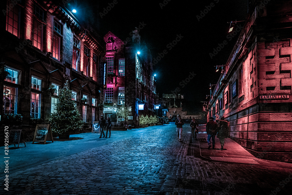 EDINBURGH, SCOTLAND DECEMBER 13, 2018: People walking along Victoria St. and Ramsay Lane, at night surrounded by colorful illuminated buildings with castle in the background.