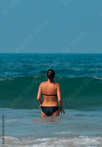 A beautiful girl in a black bikini standing in shallow sea. © PranayChandra