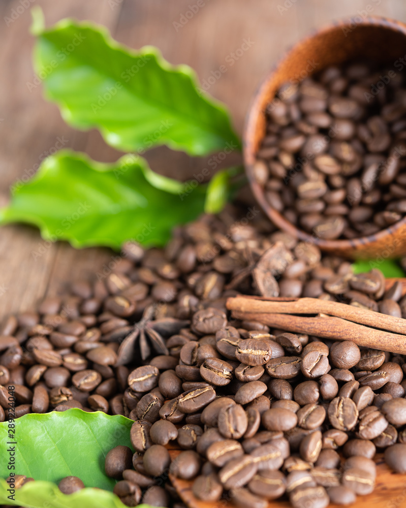 Fototapeta premium Roasted coffee beans in wood cup with green leaf star anise and cinnamon on wooden background