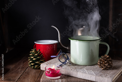Red and green coffee cup,rose candle,notebook,kettle and pine cone on wood table with dark wall background