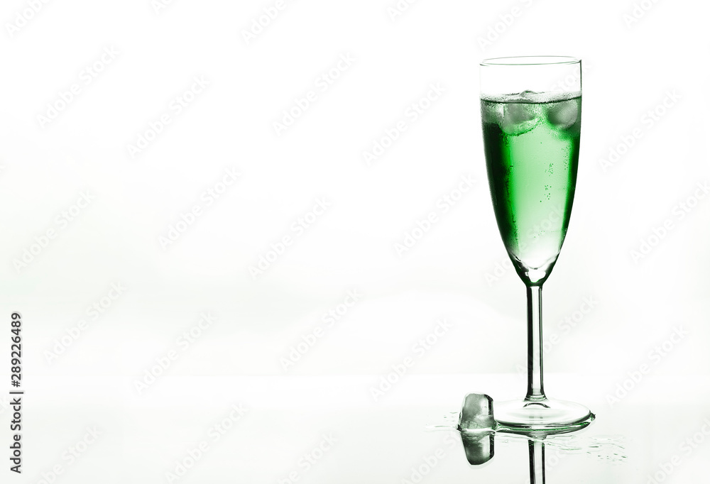 Obraz premium Glass of green champagne with ice on white background