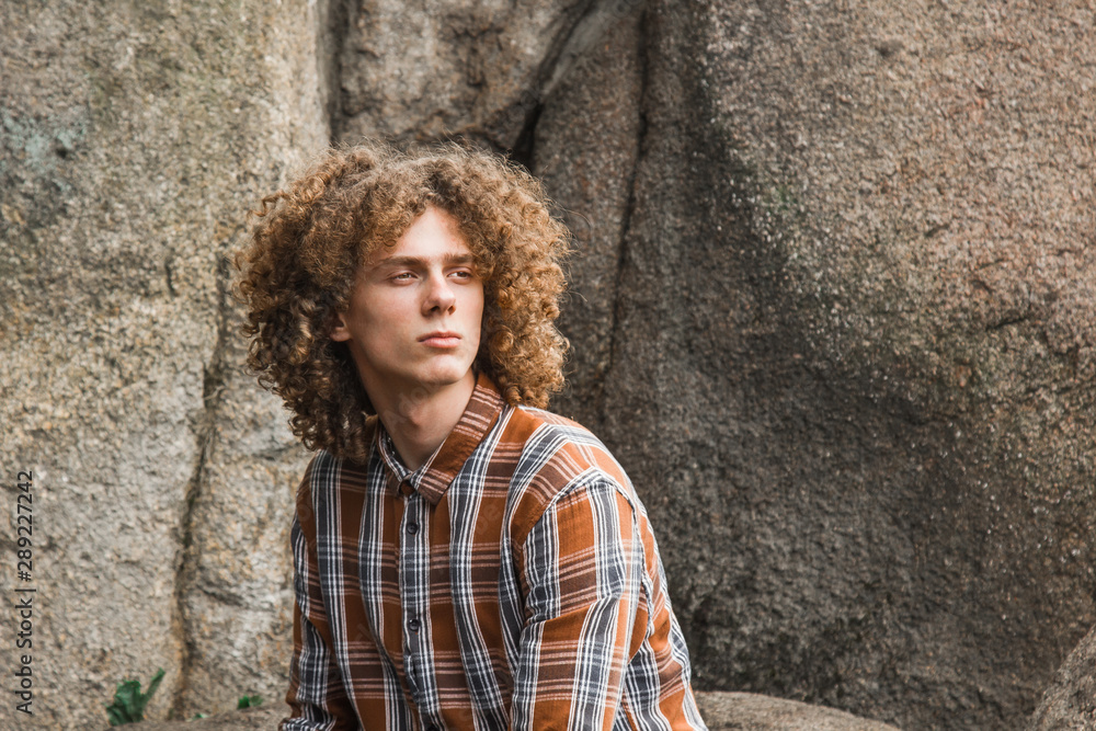 portrait of a young curly-haired guy among the stones on the street. student and young traveler concept