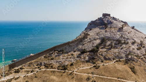 Architectural landmark, sight Of Crimea. Genoese fortress in Sudak. Aerial view of the ruins of an ancient castle or fortress on a mountain by the sea. Beautiful summer tourist landscape  © tgordievskaya