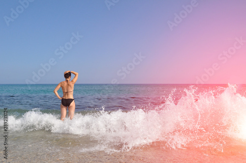 Young beautiful woman. A woman in a black swimsuit enjoys walking on the sea waves and takes sunbathing