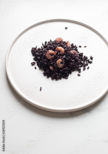 Black Italian rice Nerone in white plate on marble background with copy space
