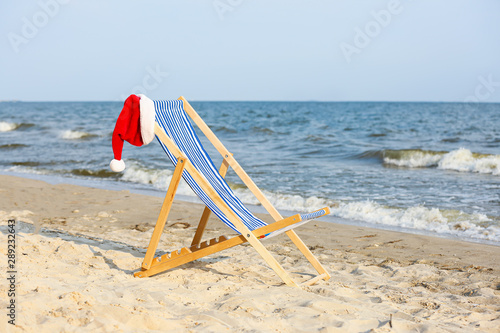 Fototapeta Naklejka Na Ścianę i Meble -  Beach chair with Santa Claus hat on sea coast. Christmas vacation