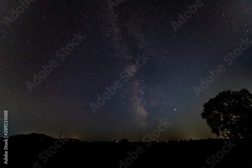 The Milky way over a black silhouette horizon with a tree.