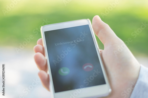Unknown caller. A woman holds a phone in his hand outdoors in a park and thinks to end the call. Incoming from an unknown number. Incognito or anonymous
