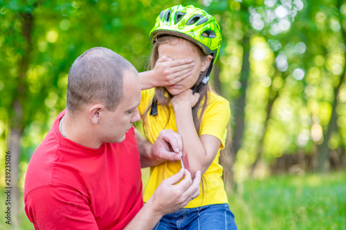 Father takes care of the little girl who fell off the bicycle, sticks a patch on the wound
