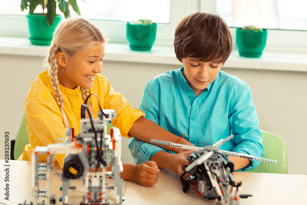 Cheerful girl playing with construction helicopter of her classmate. Cheerful girl playing with construction helicopter of her classmate.
