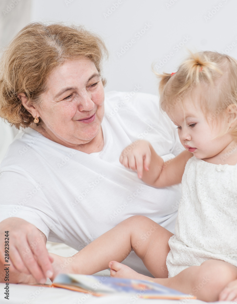 Happy family at home. Grandmother and baby girl reading a book together on the bed Happy family at home. Grandmother and baby girl reading a book together on the bed