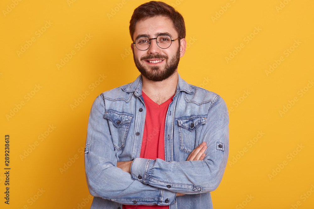 Close up portrait of bearded man with folded hands, sytanding and looking directly at camera with happy facial expression, being in good mood, handsome male dressed stylish clothing. People concept. Close up portrait of bearded man with folded hands, sytanding and looking directly at camera with happy facial expression, being in good mood, handsome male dressed stylish clothing. People concept.