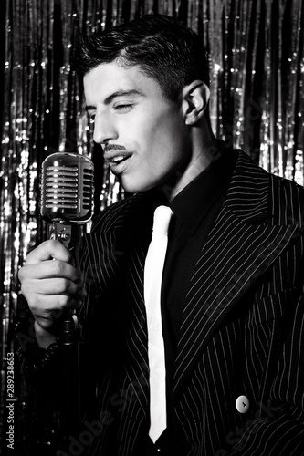 Handsome latino man singing in front of vintage microphone in nightclub with silver curtain in background photo