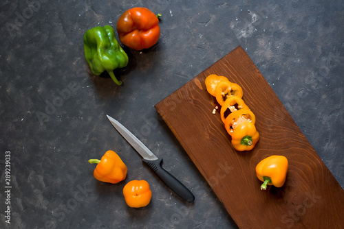 composition of fresh vegetables-cut peppers on a Board on a dark background and whole peppers orange . top view .