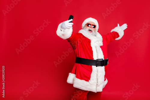 Portrait of his he nice attractive cheerful cheery positive glad friendly hospitable bearded Santa pouted lips taking making selfie blog blogger isolated over bright vivid shine red background