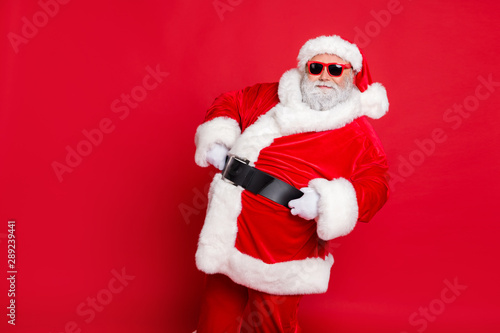 Portrait of his he nice attractive cheerful cheery content bearded Santa showing eve noel festive festal mood holding belt isolated over bright vivid shine red background