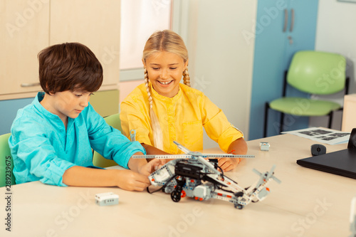 Cheerful girl looking at her classmate building a helicopter