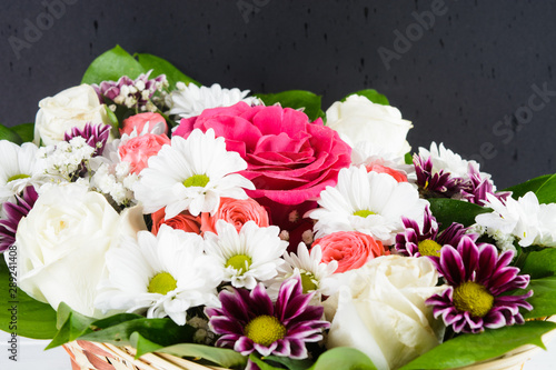 Wicker basket with roses  camomiles  chrysanthemums colorful bouquet with dark background