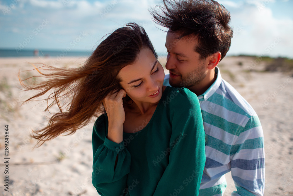 Fototapeta premium Romantic couple in love cuddling and kissing outdoors during sunset. Beautiful couple in love dating outdoors and smiling. Romantic couple on the beach.Horizontal copy space