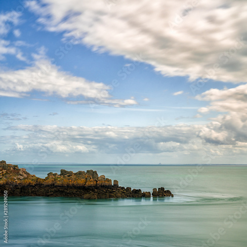 rocky cliff outcrop in a calm ocean under an expressive sky on the Emerald Coast in France photo