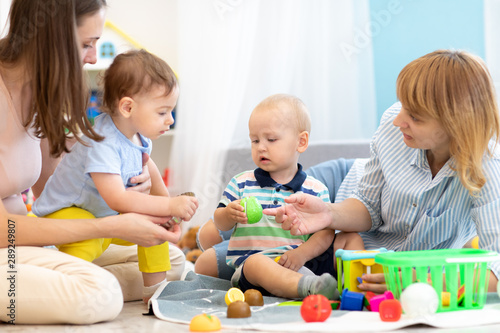 Kids playing on floor with educational toys. Toys for preschool and kindergarten. Children in nursery or daycare. Babies with teachers in creche