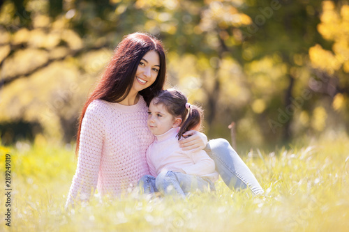 Happy mother and daughter in the autumn park. Beauty nature scene with family outdoor lifestyle. Happy family resting together on grass, having fun outdoor. Happiness and harmony in family life