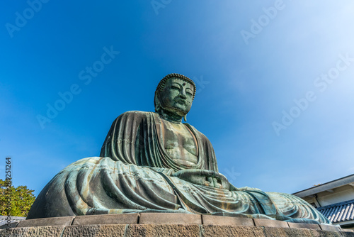 Monumental outdoor bronze statue The Great Buddha in Kamakura, Japan. Wide angle view with clear blue sky
