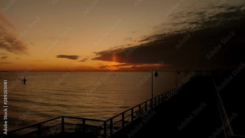 Beautiful sunrise by the sea. Orange sky and delicate clouds in the sky. Aerial footage over the wooden pier with benches and lanterns. Beautiful sunrise by the sea. Orange sky and delicate clouds in the sky. Aerial footage over the wooden pier with benches and lanterns.