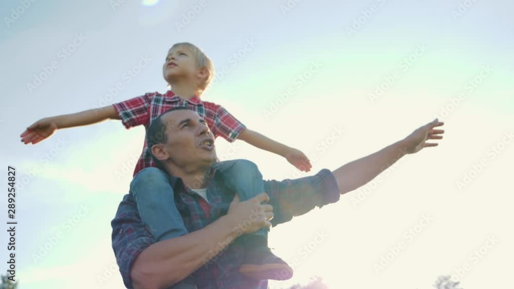 Happy family father and son play with arms wide apart. The game of the plane boy machin hands depicting the wings of an airplane. Teamwork. Family games. Happy family life concept Happy family father and son play with arms wide apart. The game of the plane boy machin hands depicting the wings of an airplane. Teamwork. Family games. Happy family life concept