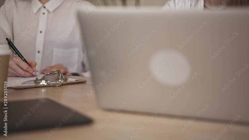 Hands of young businesswomen typing on laptop and working with documents in office while businessman passing by. Slider slow motion close up shot Hands of young businesswomen typing on laptop and working with documents in office while businessman passing by. Slider slow motion close up shot