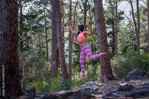 Beautiful athletic woman surrounded by trees in a forest levitating in mid air at sunrise.