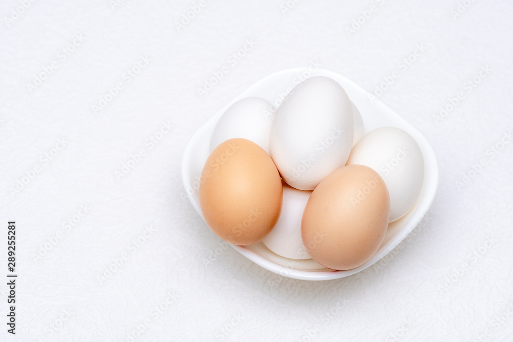 Close up shot of whole white and brown eggs in a white bowl Close up shot of whole white and brown eggs in a white bowl