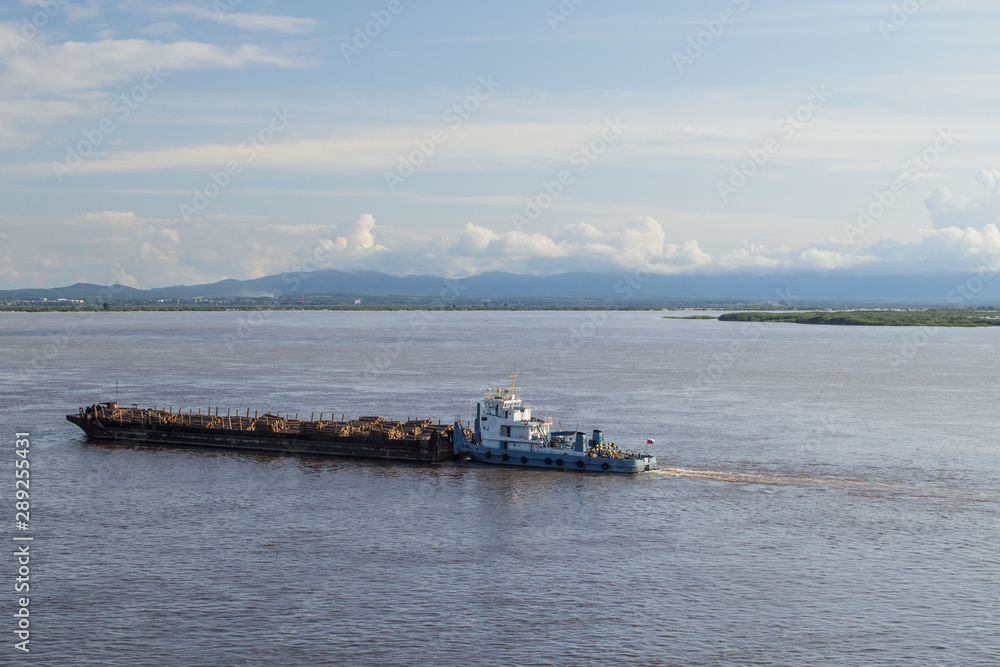On Amur River, tugboat pushes barge with forest